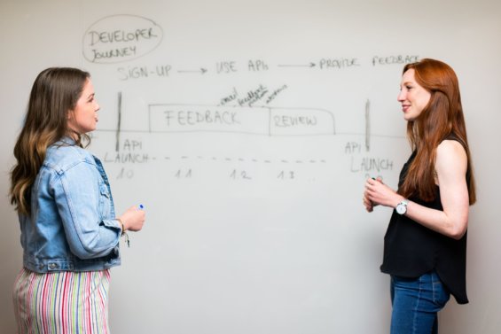 Two women talk in-front of whiteboard.