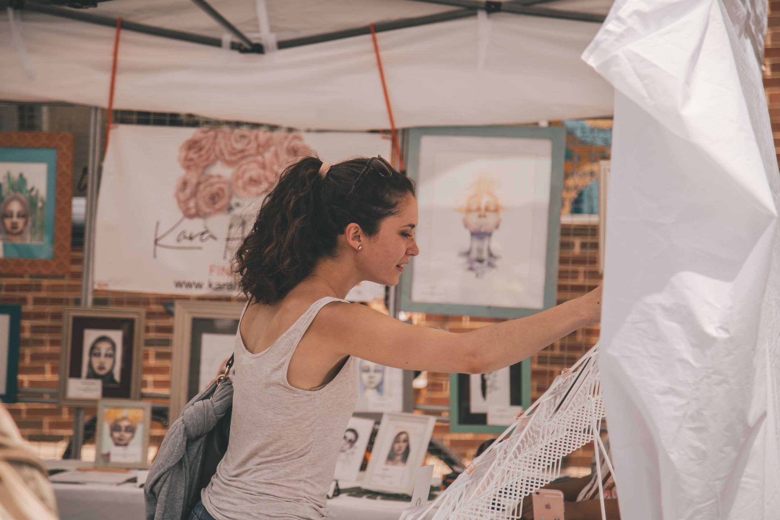Woman enjoys an artist's booth in a white tent outside.