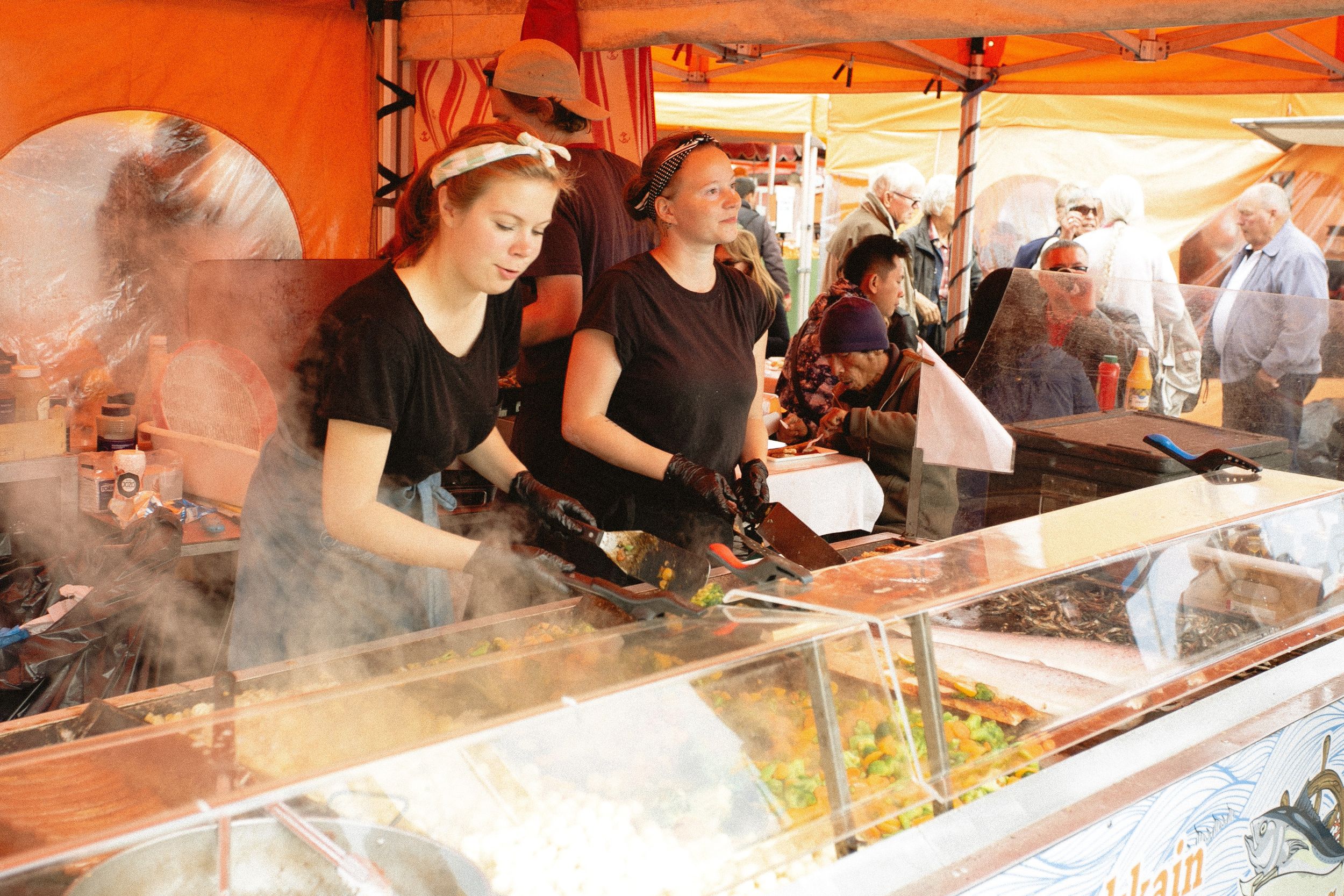 Women in black shirts sell seafood from festival stall.