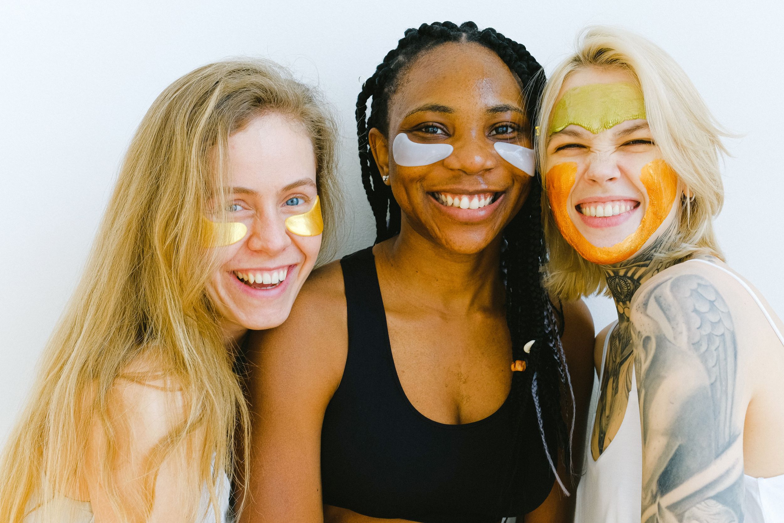 Three women smile while doing face masks.