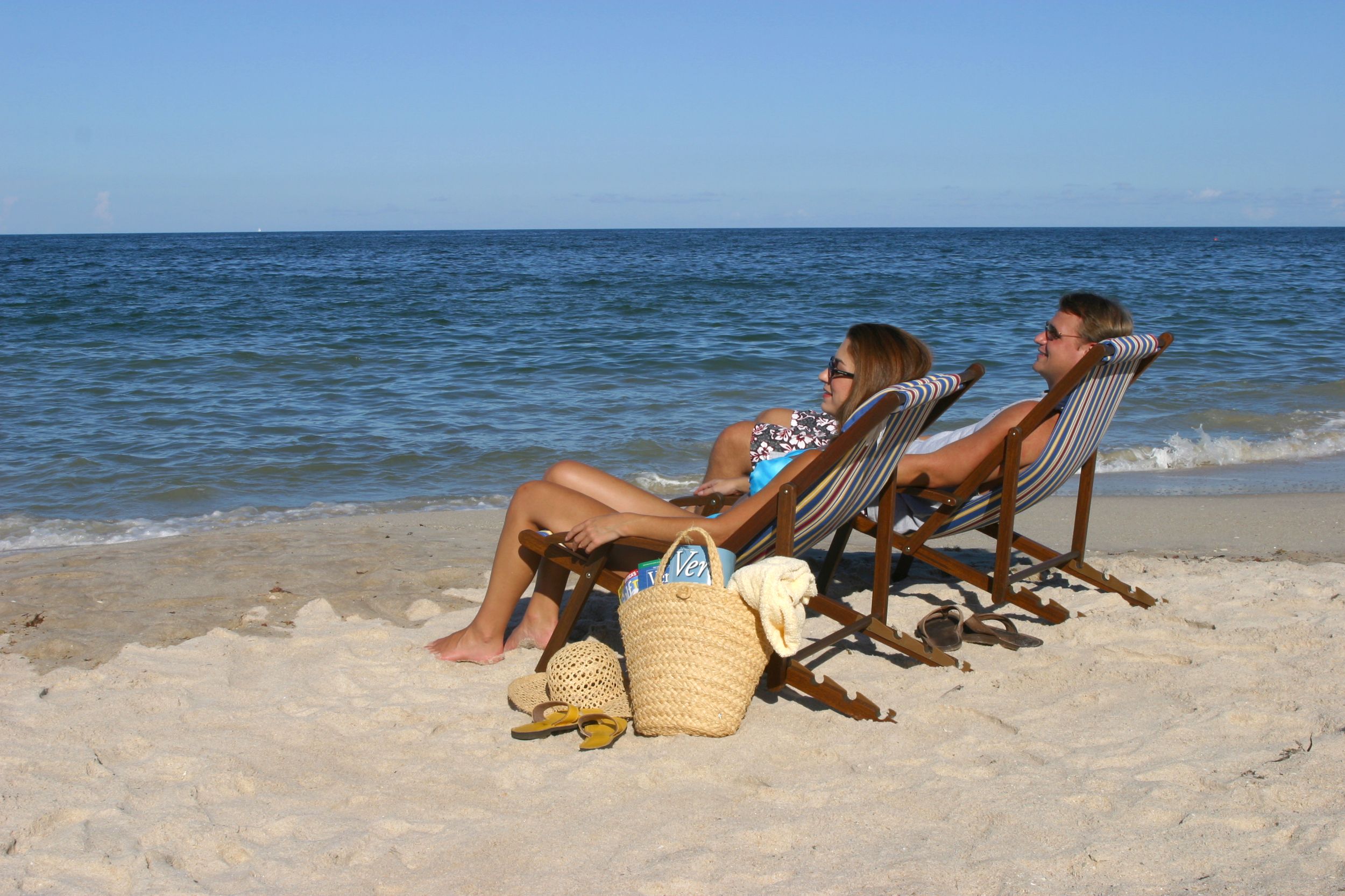 Two people recline in beach chairs on an uncrowded beach.