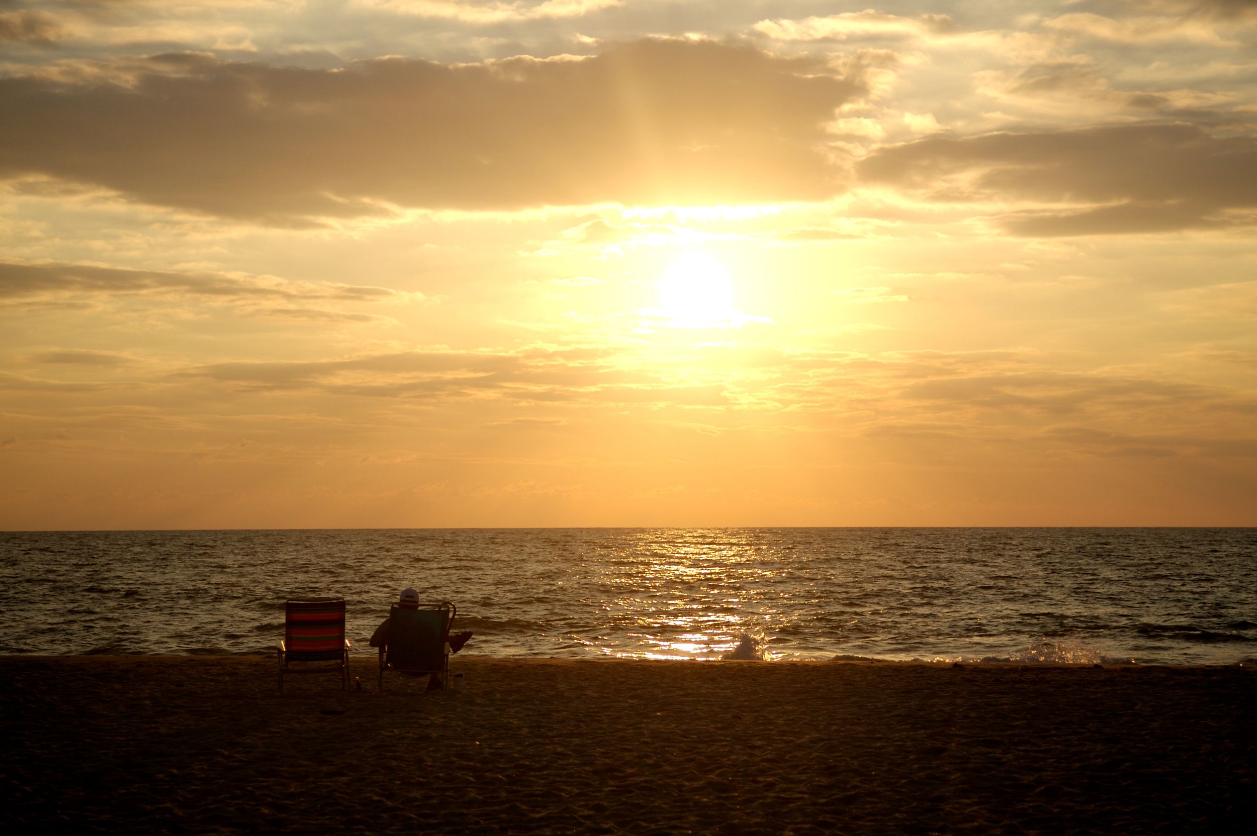 Two people sitting in beach chairs and enjoying the sunset.
