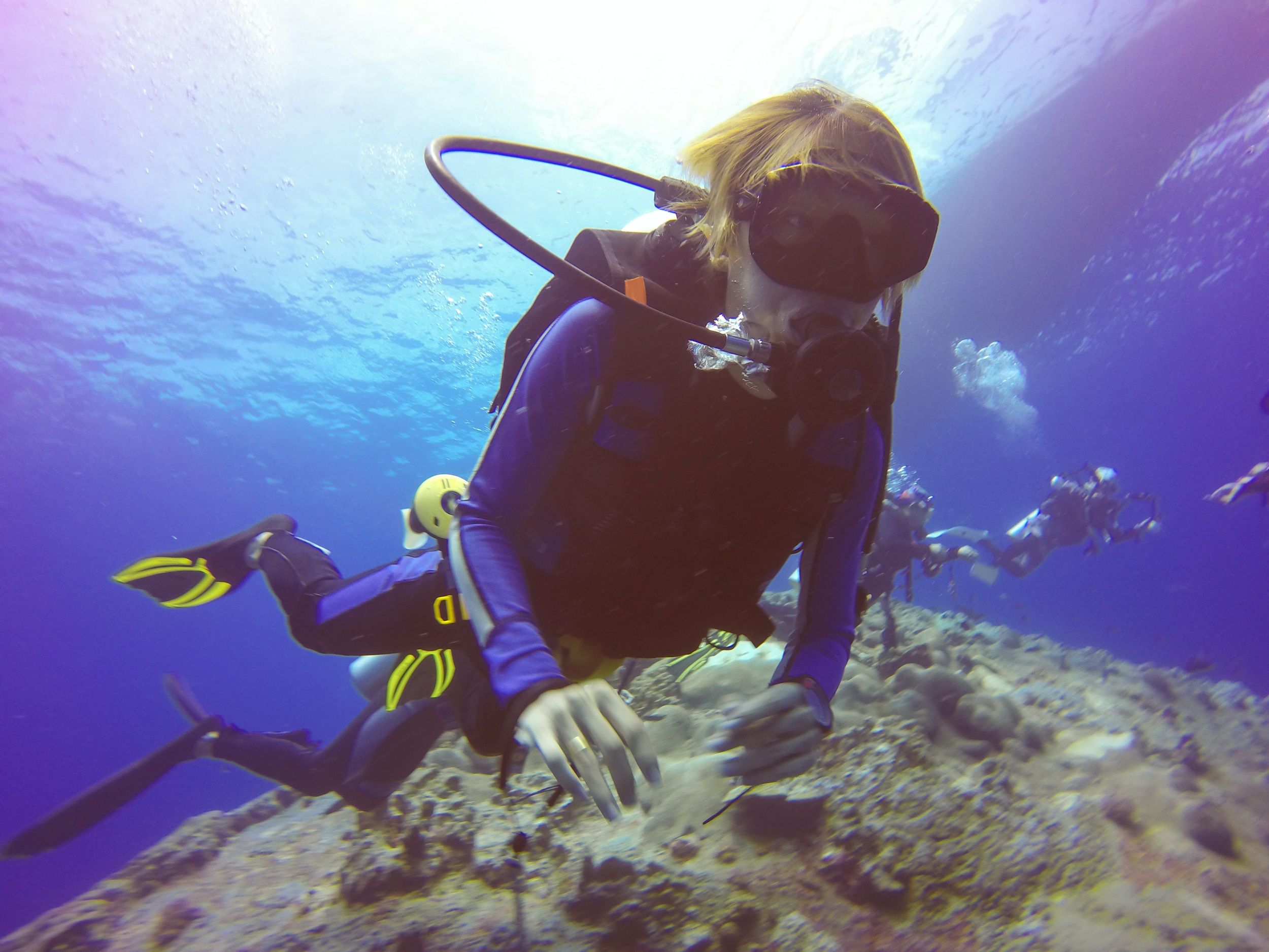 Young person scuba dives near reef.