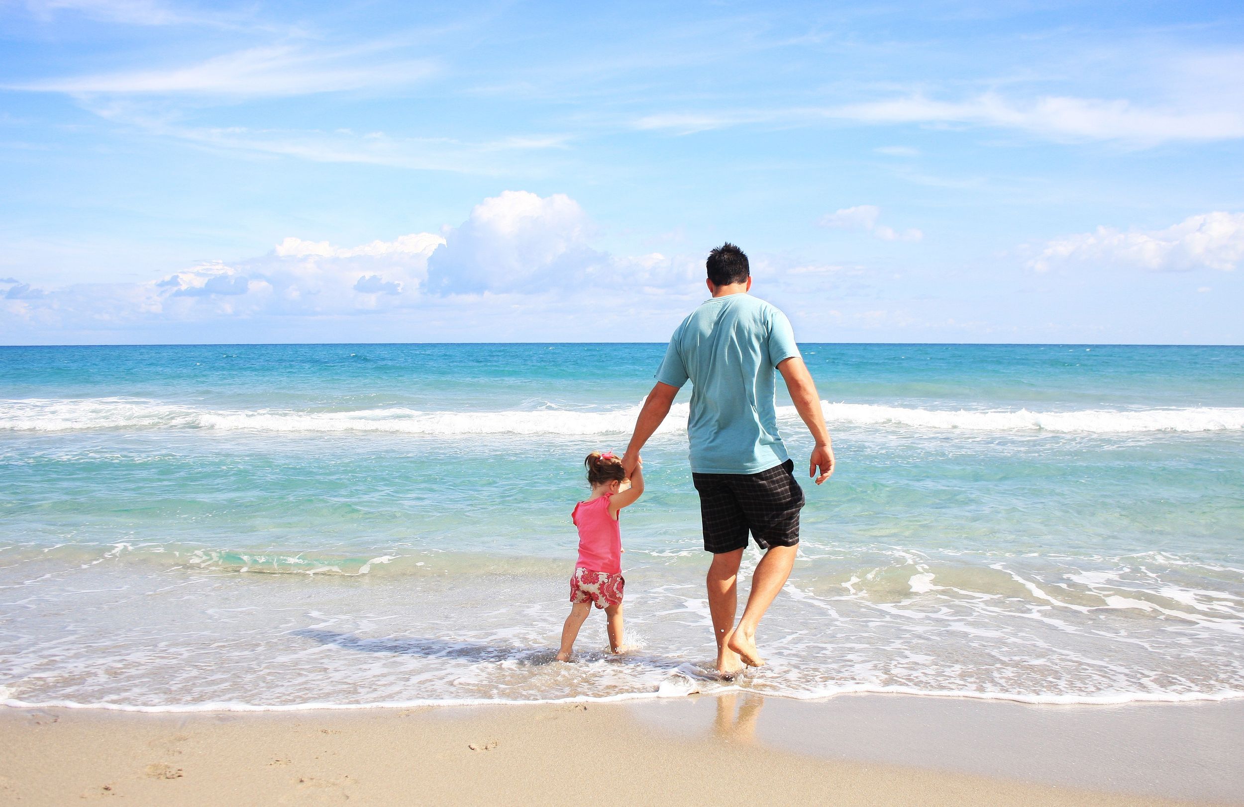 Father and daught walk hand-in-hand on the beach.